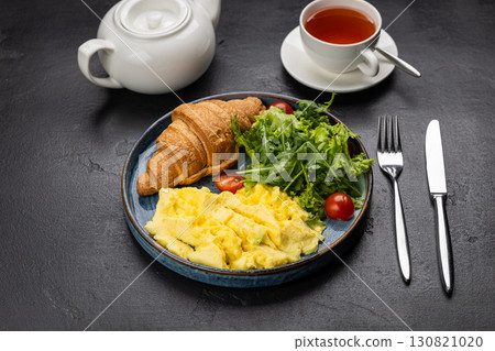 Healthy breakfast with scrambled eggs, croissant, and fresh salad on dark background 130821020