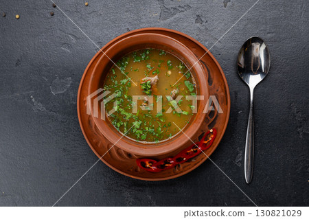 Traditional meat soup served in a clay bowl with herbs and chili on a dark background Traditional meat soup served in a clay bowl with herbs and chili on a dark background 130821029