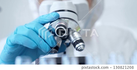 Professional scientist in protective gear is using microscope in a laboratory setting, close-up. Science and medicine concepts 130821208