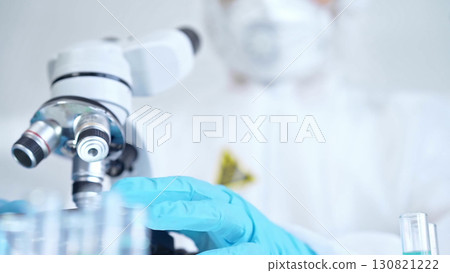 Professional scientist in protective gear is using microscope in a laboratory setting, close-up. Science and medicine concepts 130821222