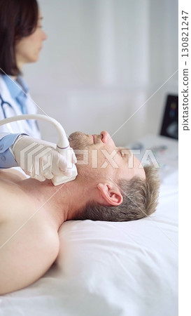 Doctor performing neck ultrasound exam on male patient 130821247