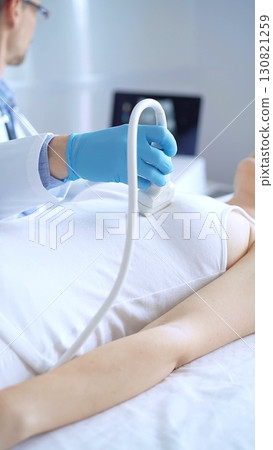 Doctor man wearing blue protective gloves is using ultrasound equipment on the breast of a female patient. Mammary gland health. Medicine concept 130821259