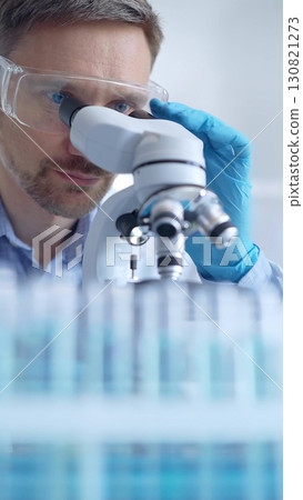 Man scientist with protective glasses and gloves is using microscope in laboratory, vertical portrait of researcher. Microbiology science concept Man scientist with protective glasses and gloves is using microscope in laboratory, vertical portrait of researcher. Microbiology science concept 130821273
