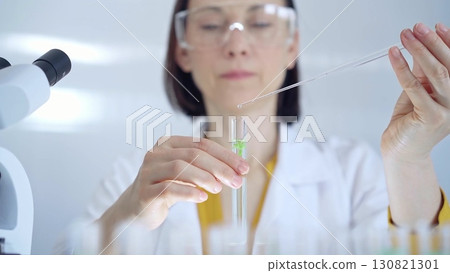 Woman with safety glasses is working with lab tubes using a pipette in a modern laboratory, close-up of researcher. Science and medicine Woman with safety glasses is working with lab tubes using a pipette in a modern laboratory, close-up of researcher. Science and medicine 130821301