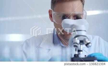 Man scientist with protective glasses and gloves is using microscope in laboratory, portrait of researcher. Microbiology science concept Man scientist with protective glasses and gloves is using microscope in laboratory, portrait of researcher. Microbiology science concept 130821304