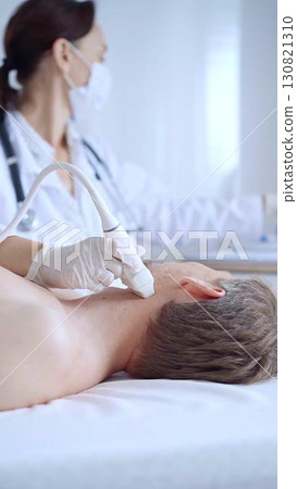Doctor woman with white medical gloves performing neck ultrasound exam on male patient. Thyroid gland examination. Medicine concept 130821310