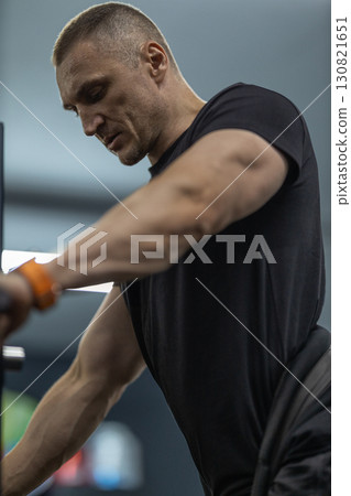 Athletic man focuses on his form while performing squats in a gym during a workout session. The environment is equipped with various fitness equipment and weights. 130821651