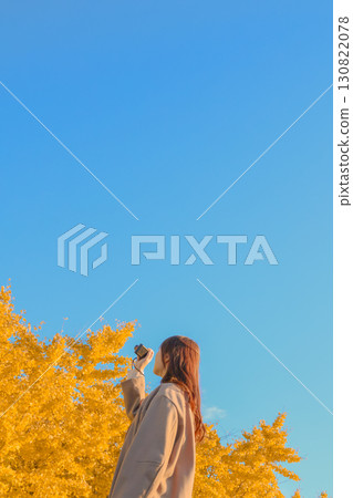 一位女士正在拍攝秋日的天空和銀杏樹 130822078