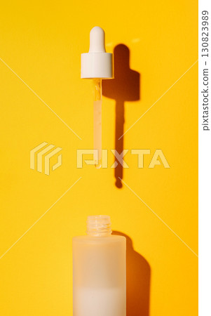 White dropper above frosted cosmetic bottle on yellow background White dropper above frosted cosmetic bottle on yellow background 130823989
