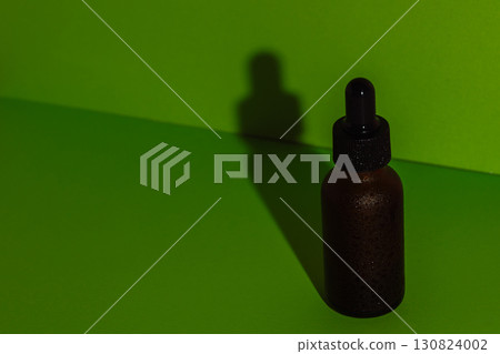 Brown dropper bottle with water drops on green background Brown dropper bottle with water drops on green background 130824002