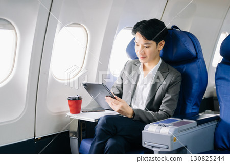 Young Asian executive excels in first class, multitasking with digital tablet, laptop and smartphone. Young Asian executive excels in first class, multitasking with digital tablet, laptop and smartphone. 130825244