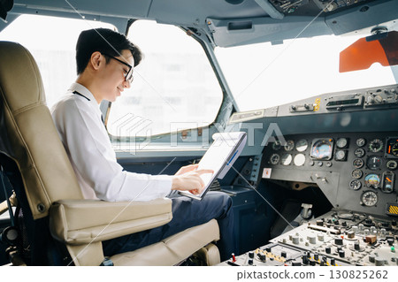 Asian Confident male pilot in uniform leaning at the passenger seat while standing inside of the airplane flight 130825262