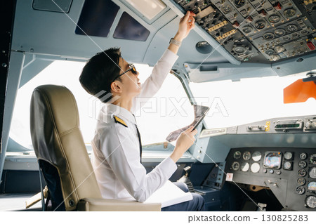 Asian Confident male pilot in uniform leaning at the passenger seat while standing inside of the airplane flight 130825283