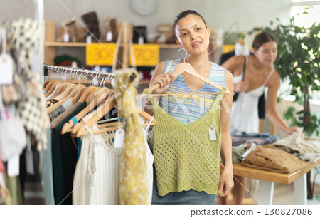 Positive young Asian woman choosing something for summer in clothing store 130827086