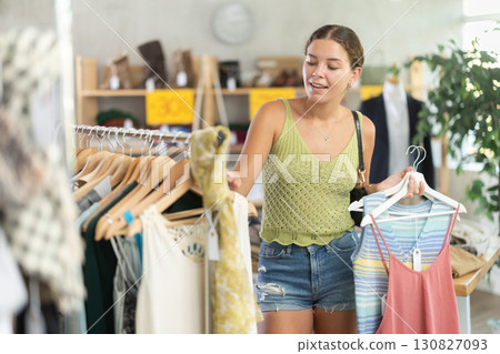 Positive young woman choosing something for summer in clothing store Positive young woman choosing something for summer in clothing store 130827093