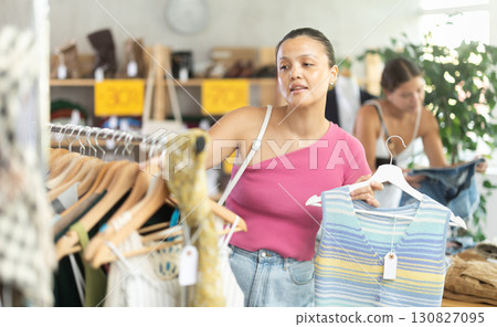 Attentive young Asian woman choosing something for summer in clothing store 130827095