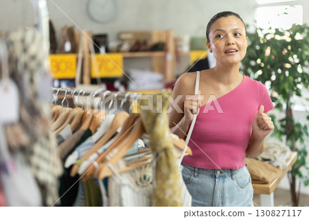 Positive young Asian woman choosing something for summer in clothing store Positive young Asian woman choosing something for summer in clothing store 130827117