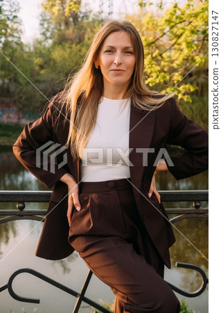 Female confidence. Outdoor portrait. Independent smiling business woman wearing suit posing in spring park at river bank. 130827147