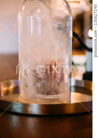Preparing alcoholic beverage. Pub glassware. Cocktail covered with transparent dome on bar counter. Smoking gun device for flavor. 130827148