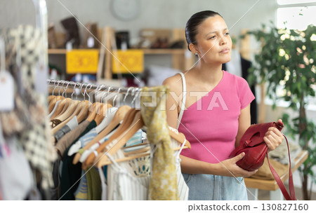 Near rack, Asian woman buys lady handbag, choose some items. Near rack, Asian woman buys lady handbag, choose some items. 130827160