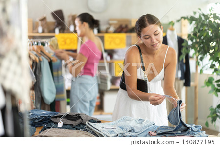 Girl customers choose trousers or shorts in store. Female client looking for something in background 130827195