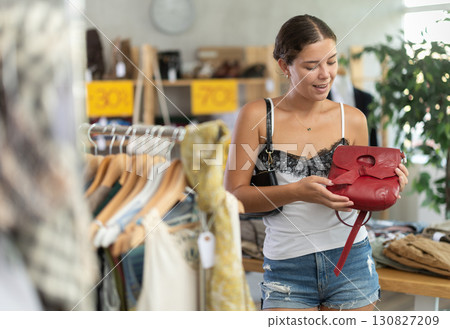 Near rack, girl buys lady handbag, choose some items. Near rack, girl buys lady handbag, choose some items. 130827209