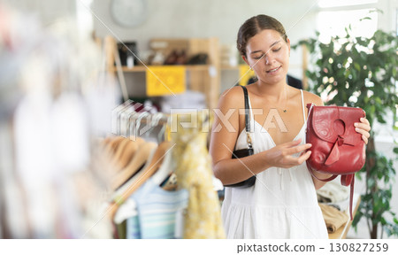 Happy young woman choosing handbag in clothing store 130827259