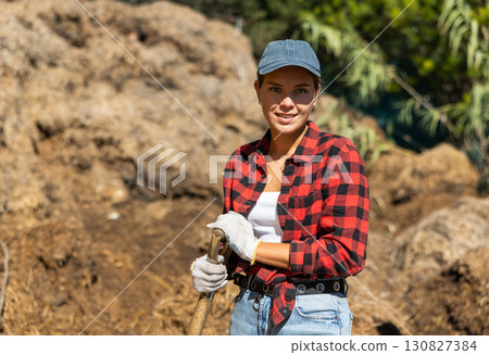Young woman with rake of pile of manure Young woman with rake of pile of manure 130827384