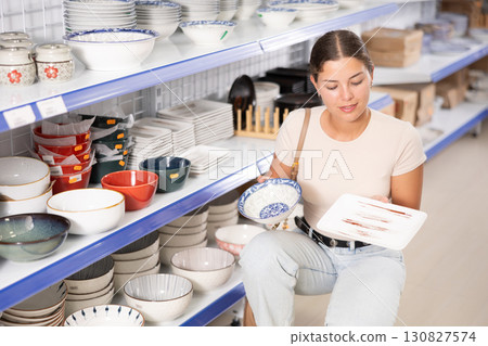 Young female shopper choosing ceramic plates at Asian store Young female shopper choosing ceramic plates at Asian store 130827574