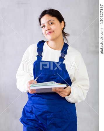 Interested female mechanic in blue overalls writing down order Interested female mechanic in blue overalls writing down order 130827587