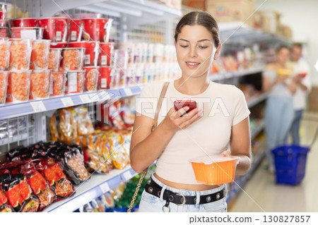 Girl scanning QR code on cup of instant noodles with smartphone in store 130827857
