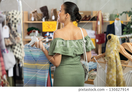 Positive asian woman choosing something for summer in clothing store 130827914