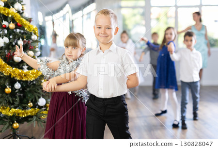 Group of preteen children in festive clothes dances waltz around Christmas tree Group of preteen children in festive clothes dances waltz around Christmas tree 130828047