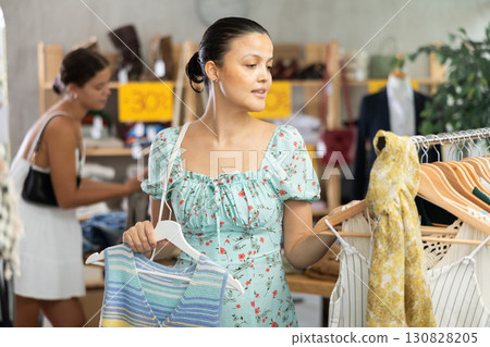 Attentive young Asian woman choosing something for summer in clothing store 130828205