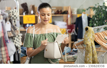 Young woman shopping - choosing fashionable handbag in clothing store 130828338