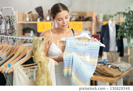 Young woman customer turn over and choose tank top in store 130828348