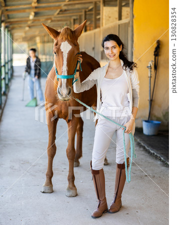 Armenian female worker takes horse out of stall, holds animal by bridle and leads pet for walk Armenian female worker takes horse out of stall, holds animal by bridle and leads pet for walk 130828354