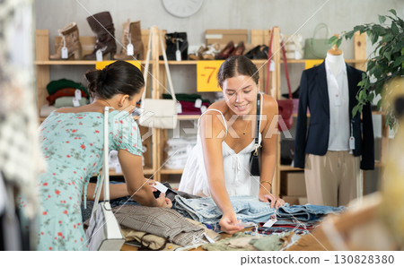 Two young women carefully choosing fashionable jeans or shorts in clothing store Two young women carefully choosing fashionable jeans or shorts in clothing store 130828380