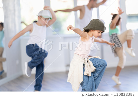 Group of happy sporty kids with male teacher training hip hop in dance studio, jumping together 130828392