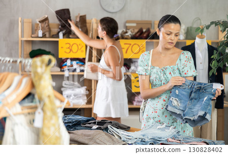 Attentive young Asian woman choosing jean shorts in clothing store 130828402