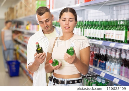Friendly young couple selecting alcoholic beverages in supermarket 130828409