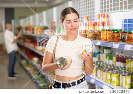 Girl choosing canned Asian vegetables in tin cans in store 130828473