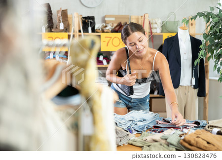 Young woman customers turn over and choose trousers or shorts in store 130828476