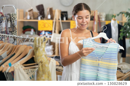 Positive young woman choosing something for summer in clothing store Positive young woman choosing something for summer in clothing store 130828629