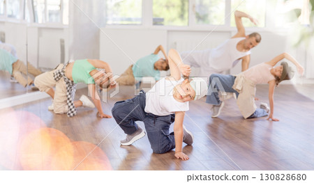 Sporty ten years old boy training breakdance movements of vigorous dance on floor during group class with male teacher in dance school 130828680