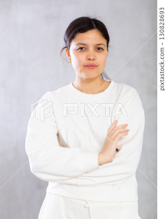 Confident young brunette standing with arms crossed on gray background 130828693