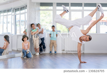 Young male coach demonstrating to group of teen children hip hop dance moves in class Young male coach demonstrating to group of teen children hip hop dance moves in class 130828705