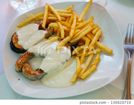 Tasty steak of fried salmon with white sauce and french fries on plate Tasty steak of fried salmon with white sauce and french fries on plate 130828710