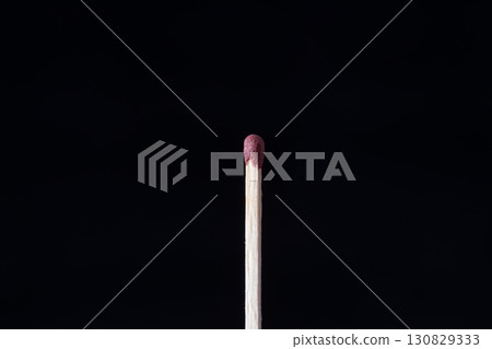 a single matchstick standing upright against a completely dark, black background 130829333