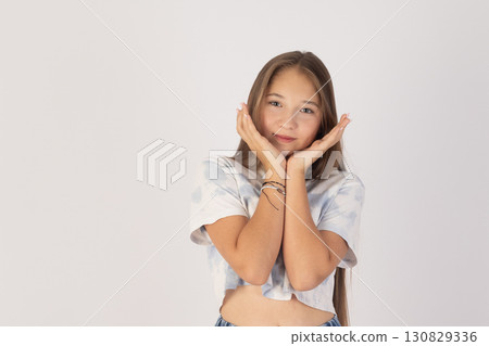 Girl is posing with her hands cupped around her face, appearing youthful and Girl is posing with her hands cupped around her face, appearing youthful and 130829336